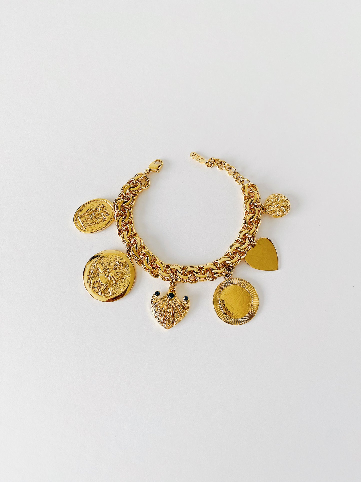 Vintage JBK Camrose & Kross gold-plated charm bracelet featuring six unique charms, including a flower, coin, palm fan with blue Swarovski crystals, Hercules disc, and an engravable heart. A Jacqueline Kennedy replica with elegant historical detailing.